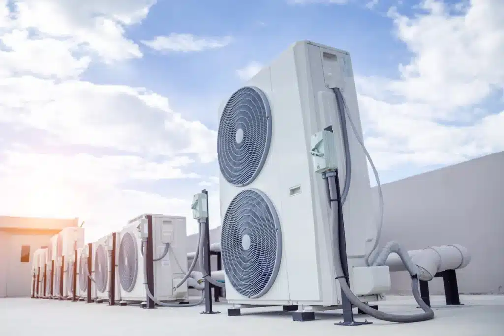 Unités Extérieures de Climatisation pour Bâtiment Industriel Alignement d'unités de climatisation extérieures sur un toit, système CVC industriel sous un ciel bleu ensoleillé.