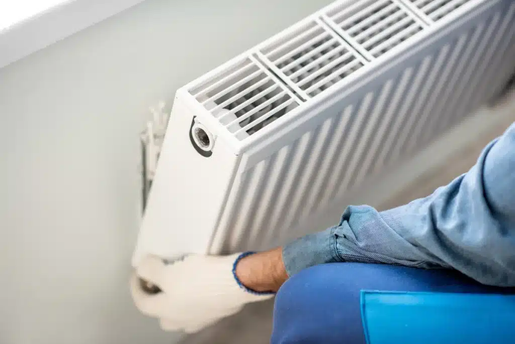 Installation de radiateur par un chauffagiste professionnel Installateur en gants blancs fixant un radiateur blanc moderne sur un mur clair pour un système de chauffage.