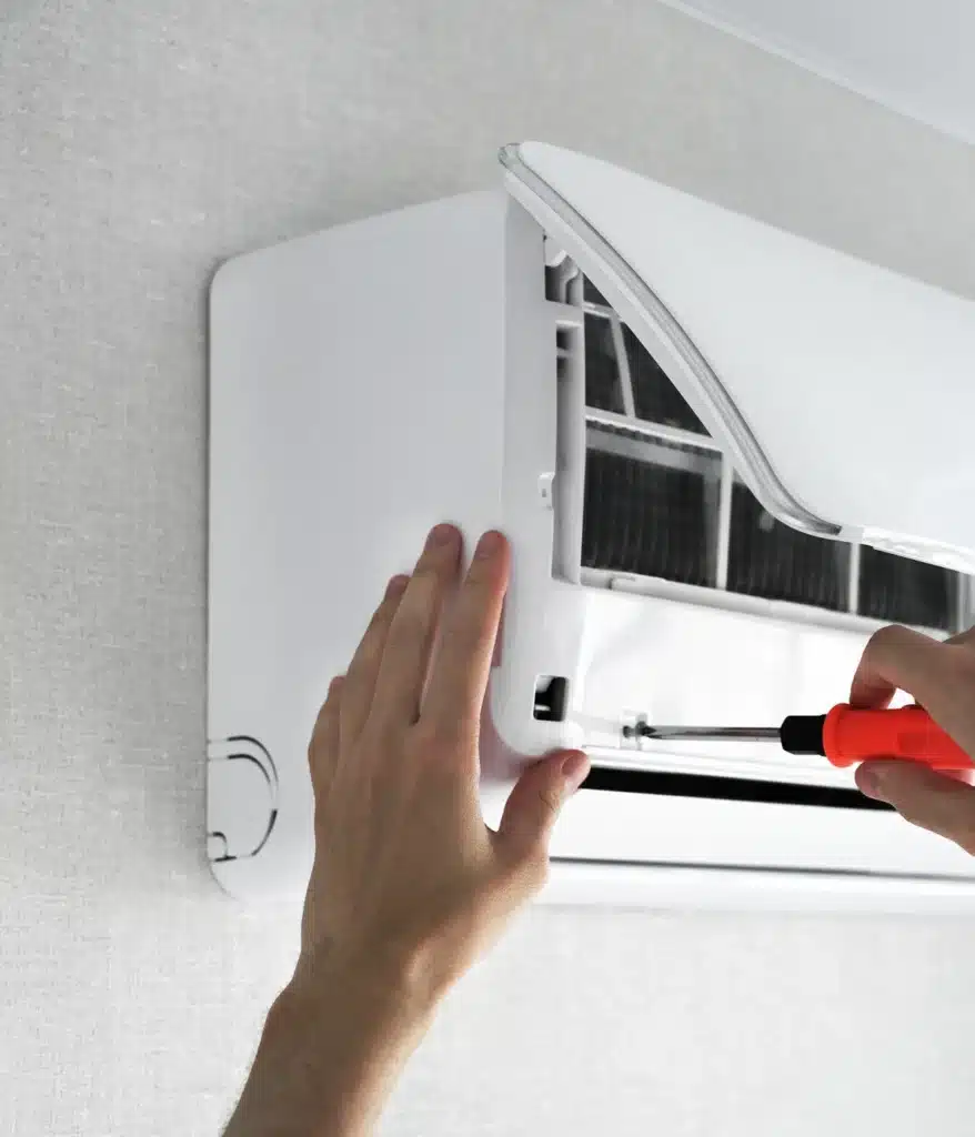 Entretien climatiseur : réparation d'un système mural Technicien réparant un climatiseur mural blanc avec un tournevis, capot ouvert pour entretien à domicile.